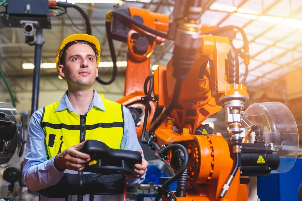 Operator bedient industriële robotarm met technische documentatie — Ecrivus International
